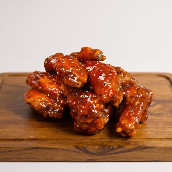 A pile of glossy, orange-glazed chicken wings topped with white and black sesame seeds on a wooden board.