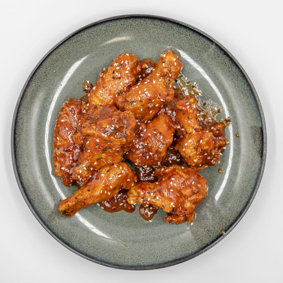 Glazed fried chicken pieces topped with black and white sesame seeds on a gray ceramic plate.