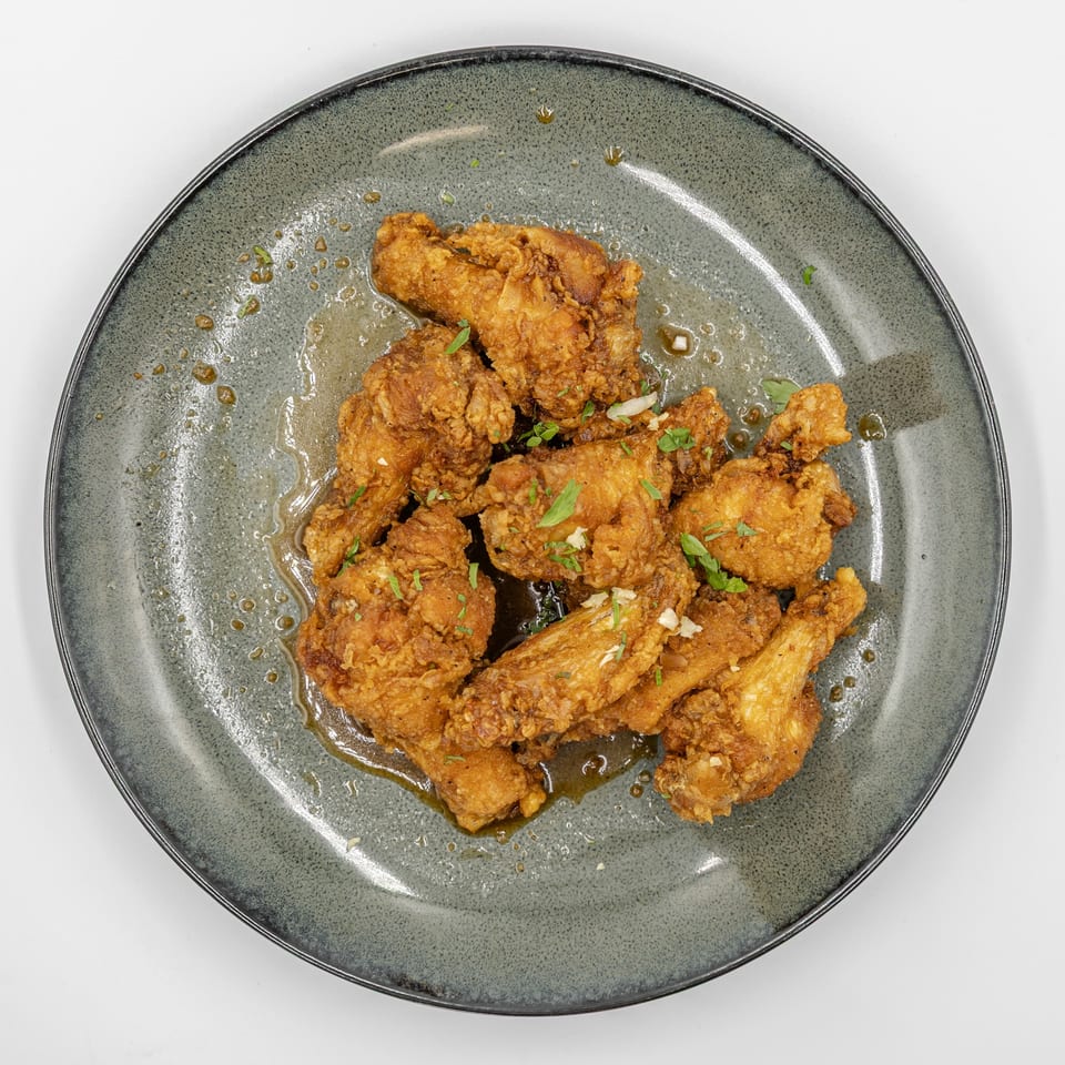 Crispy fried chicken pieces garnished with herbs and drizzled with sauce on a gray ceramic plate.