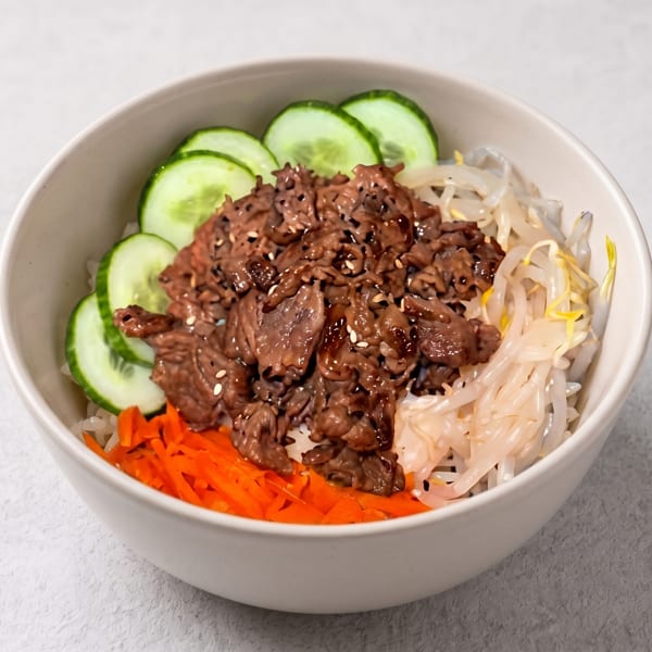 Bowl of bulgogi with rice, sliced cucumbers, shredded carrots, and bean sprouts.